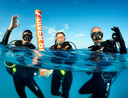 Tres buzos mostrando señal de OK durante un curso para obtener licencia de buceo.