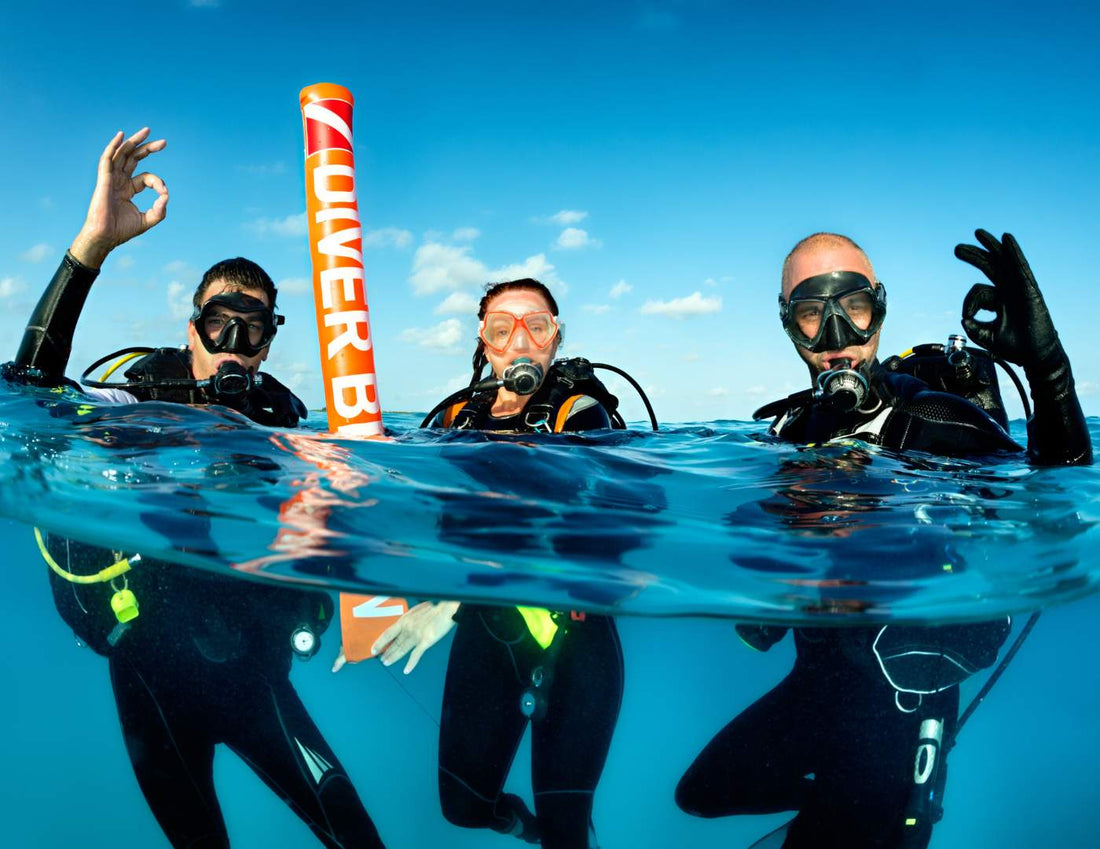 Tres buzos mostrando señal de OK durante un curso para obtener licencia de buceo.