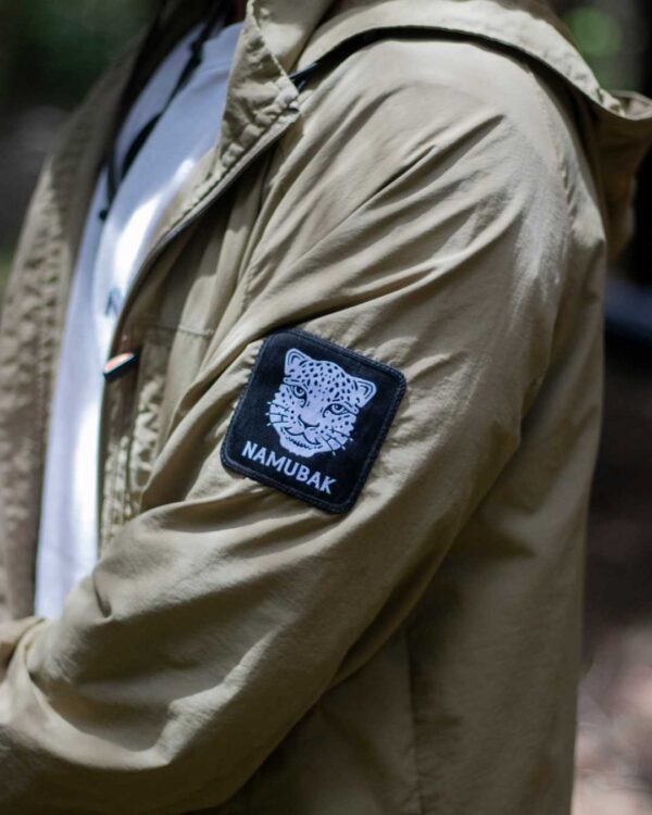 Foto de un hombre posando utilizando una Cortavientos en el Bosque. Haciendo enfoque en uno de los logos de Namubak de la Jacket