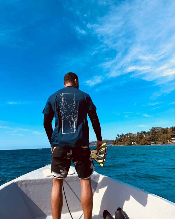 Foto de un hombre viendo el oceano en un barco y utilizando una camisa de Un Tiburon Martillo