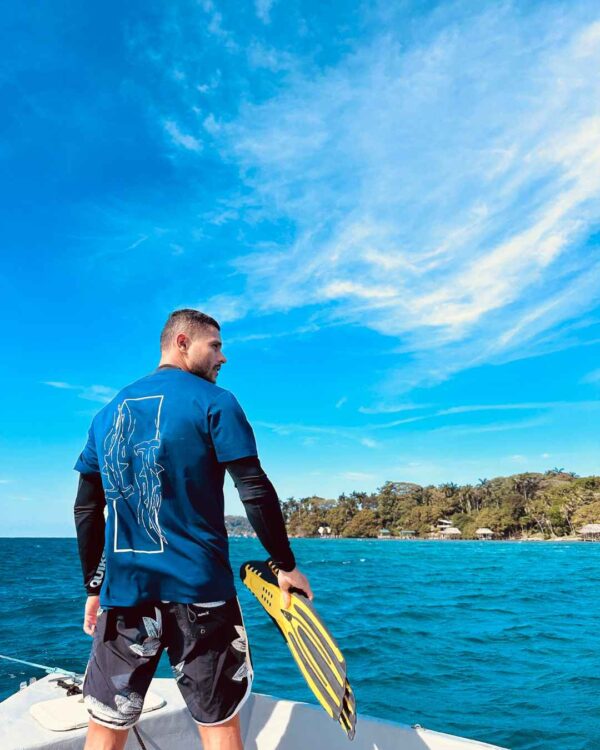 Foto de un hombre viendo el oceano en un barco y utilizando una camisa de Un Tiburon Martillo